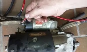 Hand hält roten Kabelanschluss an Anlasser, der mit Klemmen verbunden ist.