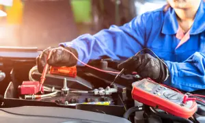 Mechaniker prüft mit Multimeter eine Autobatterie. Möglicherweise ist die **Batterie defekt**.