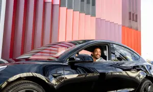 Mann lächelt im schwarzen Auto vor bunter Fassade. Ein guter Deal, der Bruttolistenpreis mit Rabatt macht es möglich.