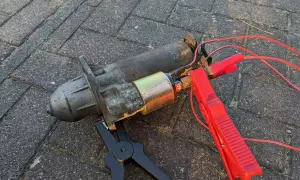 Ein defekter Anlasser, der nur klackt, liegt auf Pflastersteinen. Rote Kabel mit Klemmen sind angeschlossen.
