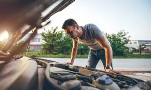 Mann beugt sich über den offenen Motorraum, weil der Motor stottert. Er sucht nach der Ursache des Problems.