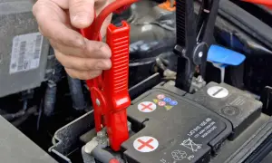 Starthilfe geben Anleitung: Rote Klemme wird an Autobatterie befestigt.