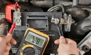 Hände prüfen mit Multimeter die Spannung der Autobatterie, um zu sehen, ob sie bereit ist, die Batterie zu laden.
