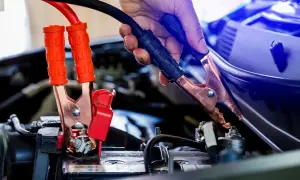 Eine Hand gibt Starthilfe, indem sie ein Überbrückungskabel an der Autobatterie befestigt.
