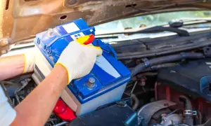 Person mit Handschuhen tauscht eine Autobatterie aus. Dies kann helfen, schwache Batterie Symptome wie Startschwierigkeiten zu beheben.