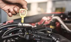 Hand prüft Ölstand am Motor eines Firmenwagens. Regelmäßige Wartung ist wichtig für die UVV.
