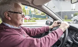 Älterer Mann fährt Auto, das beim Fahren quietscht. Er blickt konzentriert auf die Straße.