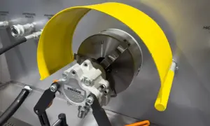 Ein defekter Servolenkungspumpe, gehalten von einer Spannvorrichtung, mit gelbem Schutzblech.
