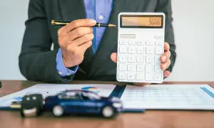 Mann mit Stift und Taschenrechner, der 9000 anzeigt. Auf dem Tisch liegen ein Auto-Schlüssel und ein Modellauto, was auf die **Erstattung Minderkilometer Leasing** hindeutet.