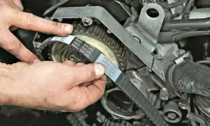 Hände montieren einen neuen Zahnriemen am Motor. So gelingt der Zahnriemenwechsel selbst.