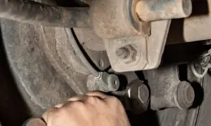 Hand mit Schraubenschlüssel am Auto-Fahrwerk. Mögliche stabilisator auto defekt symptome wie Klappern sind hier zu beheben.
