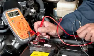 Mechaniker prüft Autobatterie mit Multimeter. Mögliche Symptome eines defekten Magnetschalters werden untersucht.