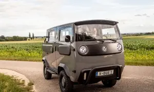 Grauer X-Bus 1 fährt auf Feldweg, Fahrer lächelt. Dieses Elektrofahrzeug ist ein Beispiel für moderne elektrische Verbraucher.