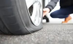 Platter Reifen am Auto. Eine Person kniet daneben und prüft den Schaden. Was tun bei reifen platt?