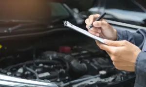 Mechaniker prüft mit Klemmbrett und Stift den Motorraum. Dies ist wichtig für die Betriebssicherheit des Autos.