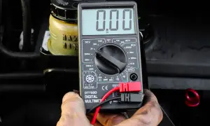 Auto springt nicht an, aber Radio geht. Ein Multimeter zeigt 0.00 an, während im Hintergrund ein Behälter mit Flüssigkeit zu sehen ist.