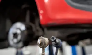 Zwei Koppelstangen liegen vor einem roten Auto. Die Koppelstange ist ein wichtiges Bauteil für die Fahrstabilität.