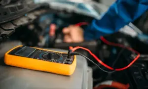 Ein Mechaniker testet die auto batterie mit einem Multimeter. Das gelbe Gerät liegt auf dem Motorraum.