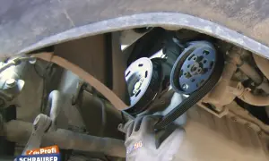 Ein Handschuh führt einen Keilriemen über Riemenscheiben. Zeit, den Keilriemen zu wechseln?