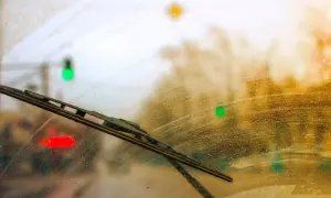 Scheibenwischer quietschen auf nasser Scheibe, während Ampeln im verschwommenen Hintergrund rot, grün und gelb leuchten.