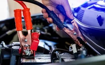 Eine Hand gibt Starthilfe, indem sie ein Überbrückungskabel an der Autobatterie befestigt.