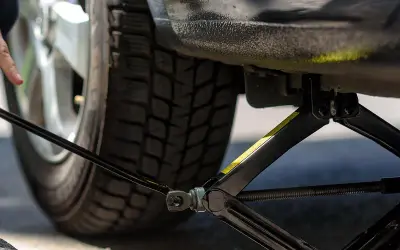 Mann hebt das Auto mit einem Wagenheber an, um neue Reifen einzufahren.