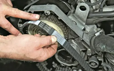Hände montieren einen neuen Zahnriemen am Motor. So gelingt der Zahnriemenwechsel selbst.