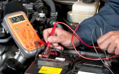 Mechaniker prüft Autobatterie mit Multimeter. Mögliche Symptome eines defekten Magnetschalters werden untersucht.