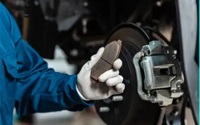 Mechaniker hält abgefahrene Bremsen in der Hand, bereit für den Austausch.