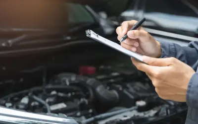 Mechaniker prüft mit Klemmbrett und Stift den Motorraum. Dies ist wichtig für die Betriebssicherheit des Autos.