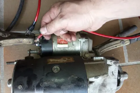 Hand hält roten Kabelanschluss an Anlasser, der mit Klemmen verbunden ist.