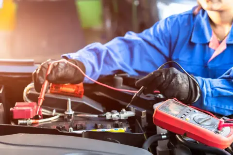 Mechaniker prüft mit Multimeter eine Autobatterie. Möglicherweise ist die **Batterie defekt**.