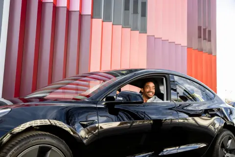 Mann lächelt im schwarzen Auto vor bunter Fassade. Ein guter Deal, der Bruttolistenpreis mit Rabatt macht es möglich.
