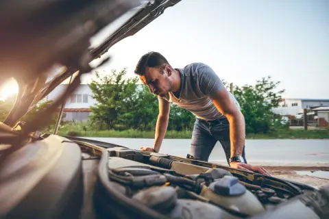 Mann beugt sich über den offenen Motorraum, weil der Motor stottert. Er sucht nach der Ursache des Problems.