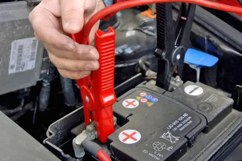 Starthilfe geben Anleitung: Rote Klemme wird an Autobatterie befestigt.