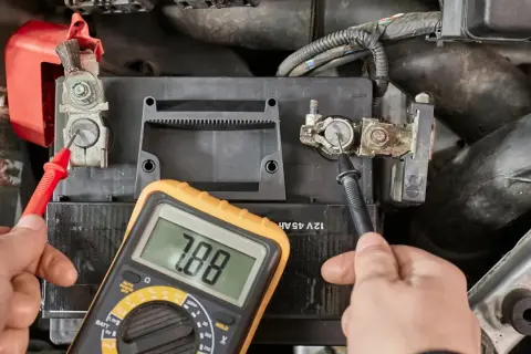 Hände prüfen mit Multimeter die Spannung der Autobatterie, um zu sehen, ob sie bereit ist, die Batterie zu laden.