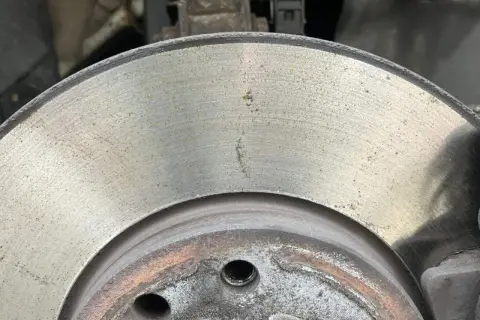 Nahaufnahme einer Bremsscheibe mit leichtem Rost. Die Oberfläche zeigt feine Rillen und einige gelbliche Spuren, die auf beginnenden Rost hindeuten.