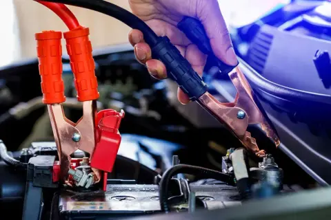 Eine Hand gibt Starthilfe, indem sie ein Überbrückungskabel an der Autobatterie befestigt.