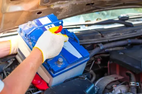Person mit Handschuhen tauscht eine Autobatterie aus. Dies kann helfen, schwache Batterie Symptome wie Startschwierigkeiten zu beheben.