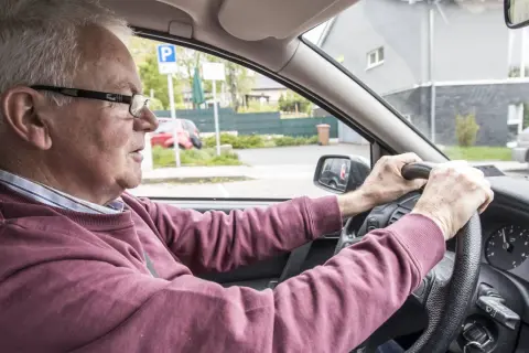 Älterer Mann fährt Auto, das beim Fahren quietscht. Er blickt konzentriert auf die Straße.