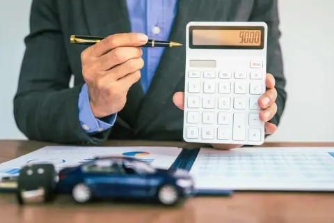 Mann mit Stift und Taschenrechner, der 9000 anzeigt. Auf dem Tisch liegen ein Auto-Schlüssel und ein Modellauto, was auf die **Erstattung Minderkilometer Leasing** hindeutet.