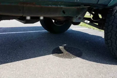 Ein Auto tropft Wasser nach der Fahrt. Eine Pfütze bildet sich auf dem Asphalt unter dem Fahrzeug.