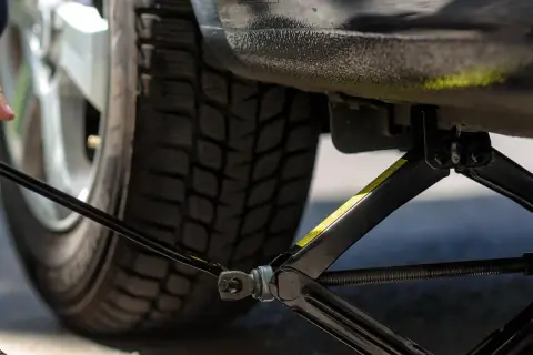 Mann hebt das Auto mit einem Wagenheber an, um neue Reifen einzufahren.