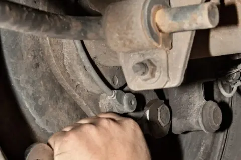 Hand mit Schraubenschlüssel am Auto-Fahrwerk. Mögliche stabilisator auto defekt symptome wie Klappern sind hier zu beheben.