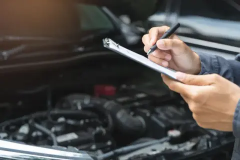 Mechaniker prüft mit Klemmbrett und Stift den Motorraum. Dies ist wichtig für die Betriebssicherheit des Autos.