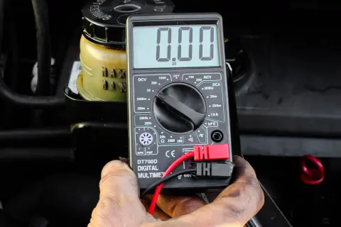 Auto springt nicht an, aber Radio geht. Ein Multimeter zeigt 0.00 an, während im Hintergrund ein Behälter mit Flüssigkeit zu sehen ist.