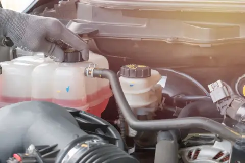 Hand in glove checks the coolant level in the car's engine. The pink liquid is the **wasser unter auto**, essential for keeping the engine cool.