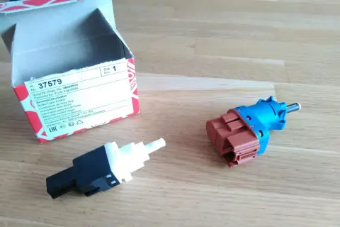 Zwei neue Bremslichtschalter liegen neben einer geöffneten Verpackung. Ein Teil ist blau und braun, das andere schwarz und weiß.