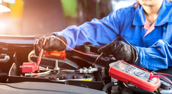 Mechaniker prüft mit Multimeter eine Autobatterie. Möglicherweise ist die **Batterie defekt**.