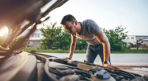 Mann beugt sich über den offenen Motorraum, weil der Motor stottert. Er sucht nach der Ursache des Problems.